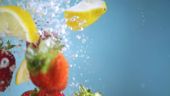 Super slow motion shot of lemon slices and strawberries falling into the water with a splash. Blue b