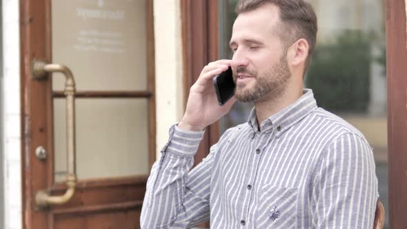 Young Man Talking on Phone while Sitting Outdoor alt