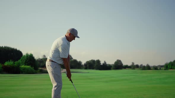 Senior Golf Player Practicing Hitting Ball on Grass Field alt