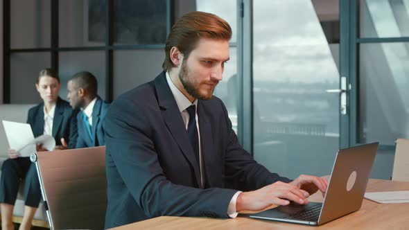 Working man in a suit with a laptop in the office. Young businessman at work alt