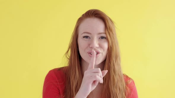funny woman with red hair presses finger to her lips makes gesture of silence