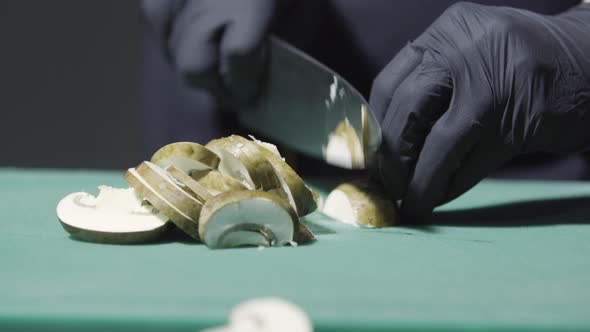 Cook's Hands in Black Gloves Slicing Mushrooms Close Up alt