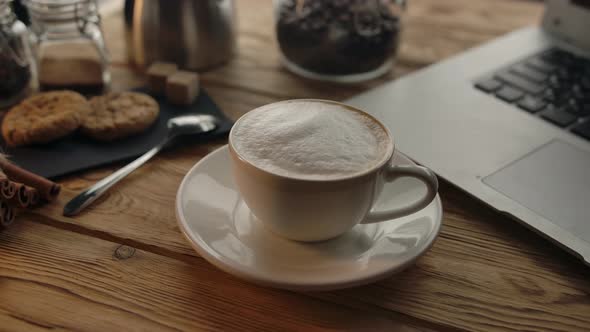A Cup of Coffee on a Wooden Table Next to a Laptop alt