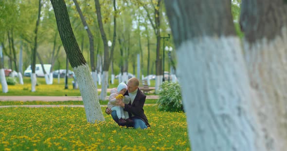 Baby Girl is Spending Time with Her Dad in Park in Springtime Resting on Dandelion Lawn  Prores