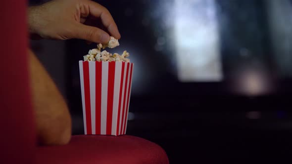 Eating popcorn while watching a movie on the couch at home.