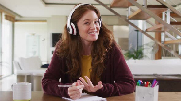 Caucasian woman sitting at desk wearing headphones having video call smiling alt