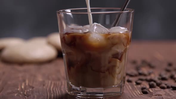 Slow Motion of Cream Being Poured Into a Glass of Cold Brew Iced Coffee on Brown Wood Table with