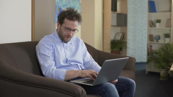 Man With Eyeglasses Sitting on Sofa and Shopping Online on Laptop, Technologies alt