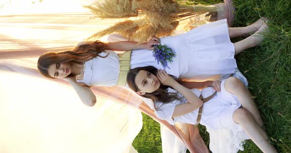 Two Girl Teenagers in White Dresses with Flowers Bouquet Posing on Chifon Background in a Field at alt