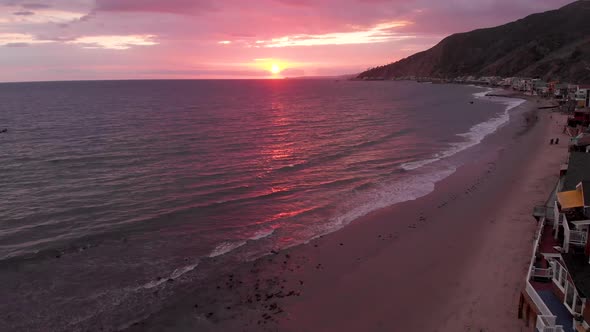 Drone flies by expensive houses revealing Sunset over ocean near Malibu