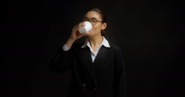 Brunette in Glasses and Office Clothes Drinks Coffee From a White Paper Cup alt