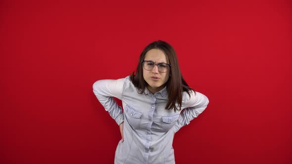 A Young Woman with Glasses Has a Backache and Is Holding It in Her Hands alt