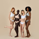 Happy diverse young women wearing underwear standing on beige background.  Stock Photo by insta_photos