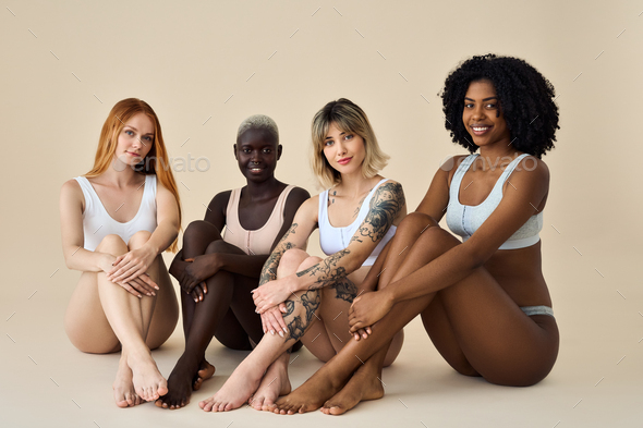 Happy diverse young women wear underwear sitting showing legs on