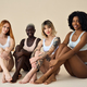 Diverse young women wear underwear sitting showing legs on beige  background. Stock Photo by insta_photos