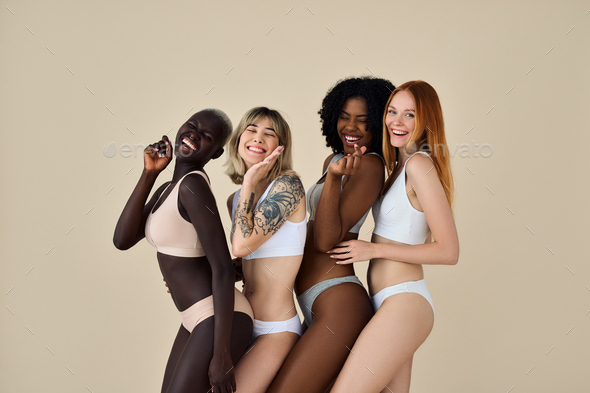 Happy pretty diverse girls wearing underwear dancing on beige