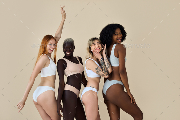 Happy multicultural girls wearing underwear dancing on beige