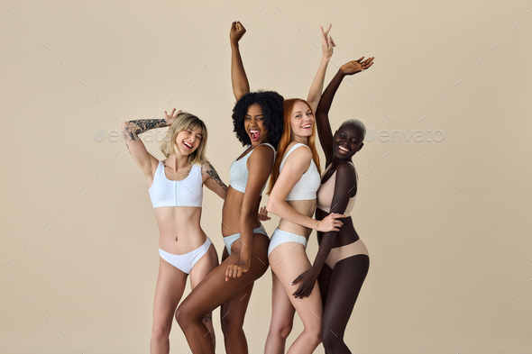 Happy diverse young women wearing underwear dancing on beige