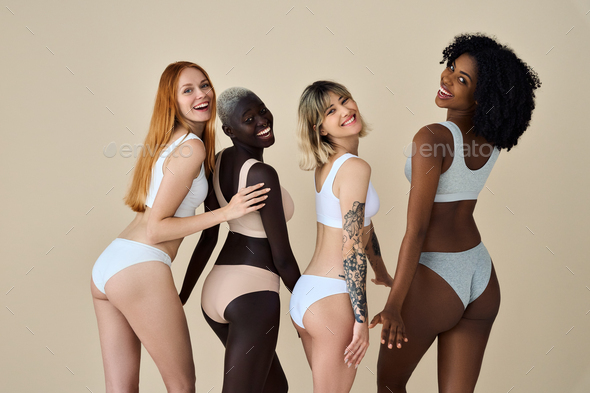 Happy diverse young women wearing underwear standing on beige