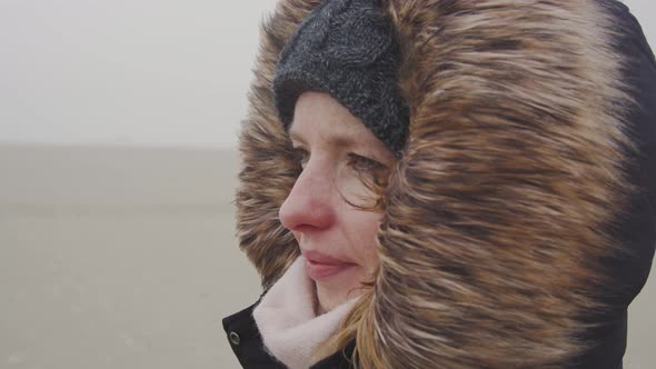 Young woman standing in the wind of a barren landscape, protected from the freezing cold with a fur alt