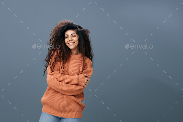 HUGS CONCEPT. Enjoyed smiling tanned curly Latin female in warm sweater cross hands hugging herself