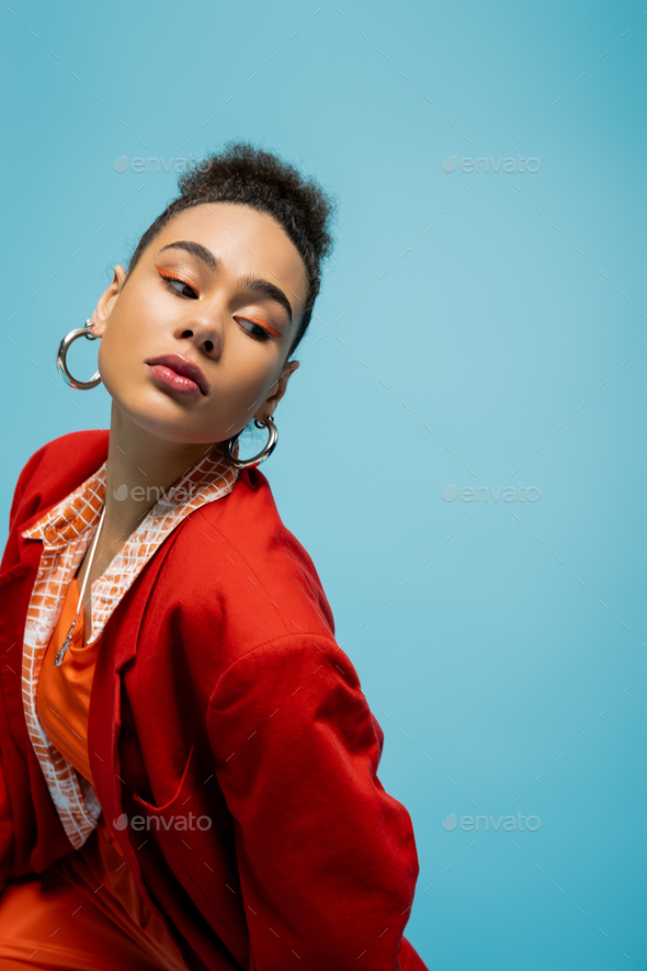 portrait of pretty fashion model in stylish red outfit with hoop earrings on blue backdrop