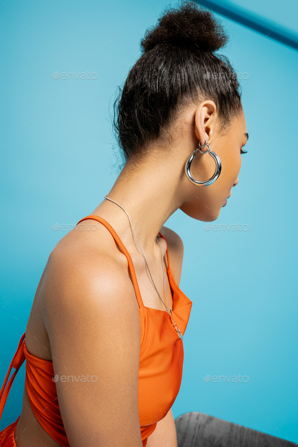 trendy african american fashion model in striking orange outfit with hoop earrings looking away
