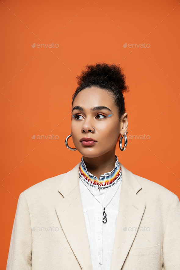 portrait of young pretty african american woman with trendy hoop earrings on orange background