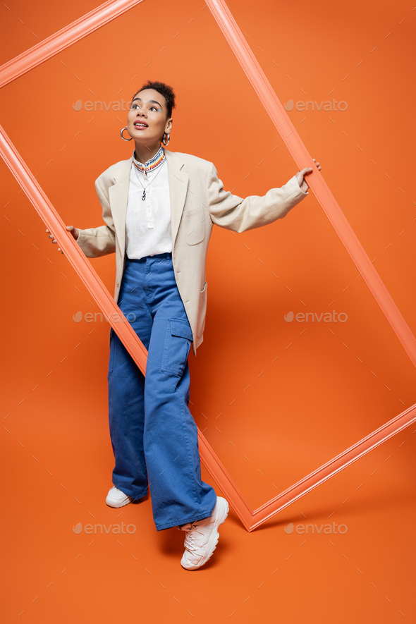 fashionable woman in beige blazer with hoop earrings and a necklace posing with orange framework