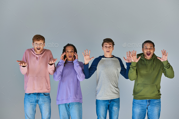 four shocked multicultural friends in colorful street attire on grey backdrop, cultural diversity