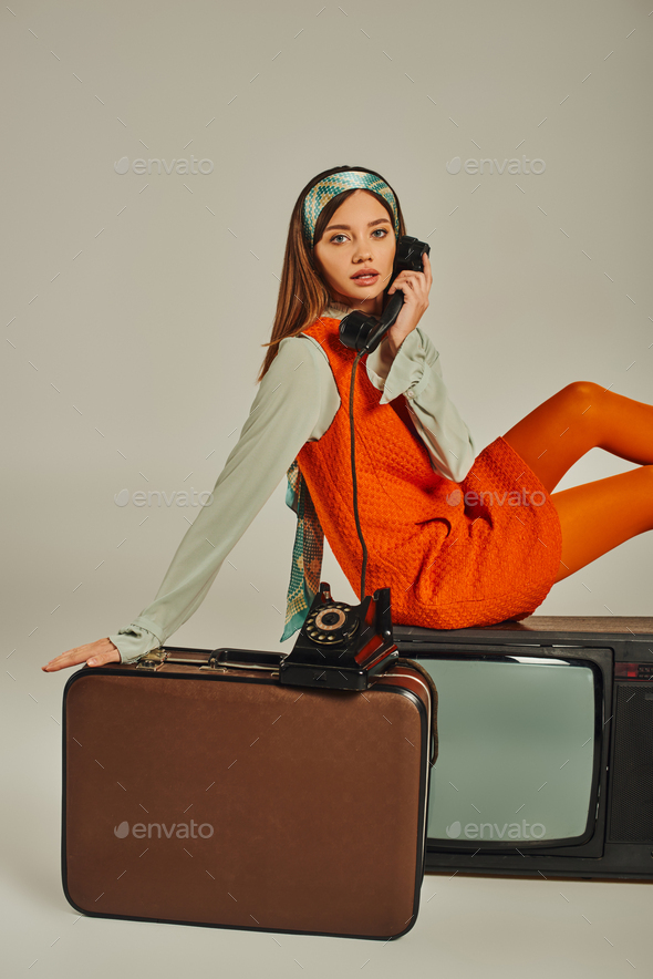 charming retro woman sitting on vintage suitcase and tv set while