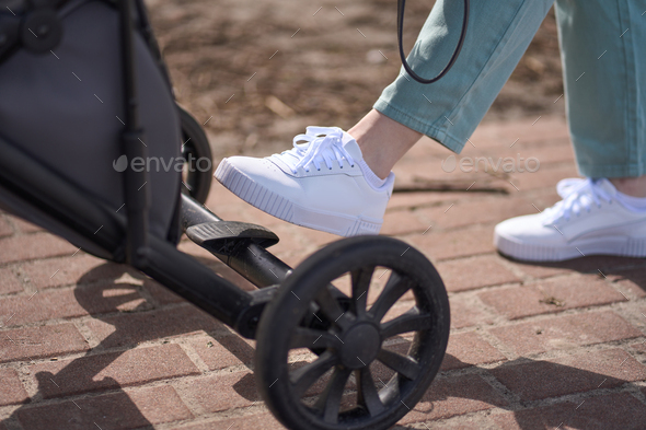 Details on female foot on the brake pedal of baby carriage during stroll outdoors
