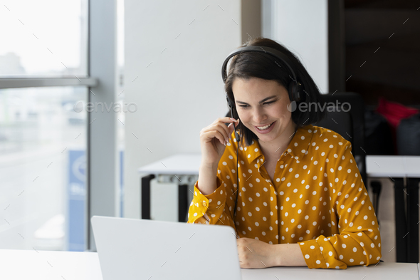 Pleasan call center manager in audio headset, sitting at table, using laptop having online meeting