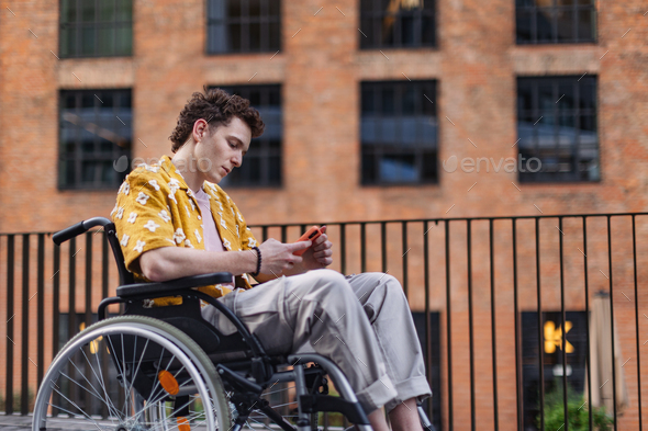 Gen Z boy in wheelchair in the city using smartphone. Inclusion, equality, and diversity among