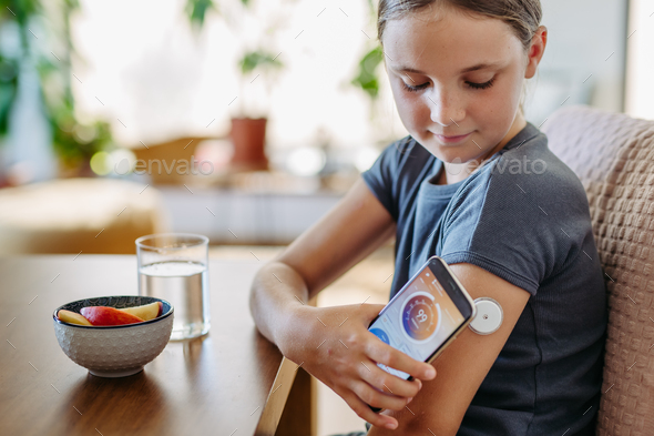 Girl with diabetes checking blood glucose level at home using continuous glucose monitor. Schoolgirl