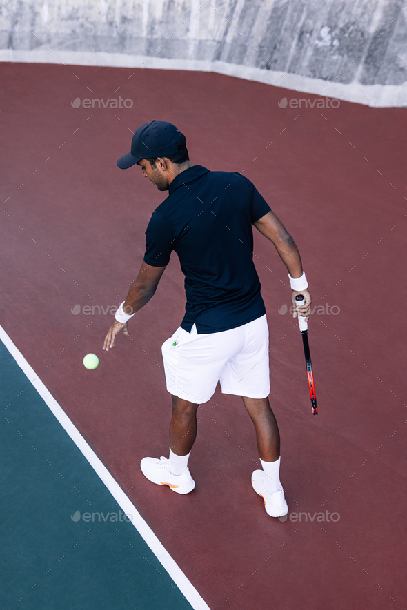 Full length of a male tennis player with ball and racket at baseline