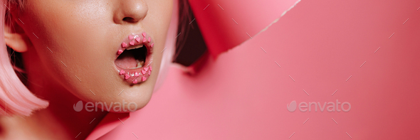 Surprised face of a girl model with bright makeup looks into a hole in pink paper
