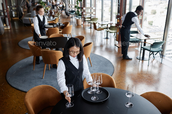 Multiethnic group of servers setting tables in restaurant preparing for guests