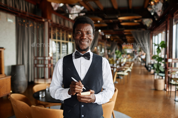 Young Black man as server in restaurant holding notepad ready to take orders
