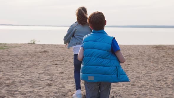 Two Children Run Along Sandy Beach To Seashore