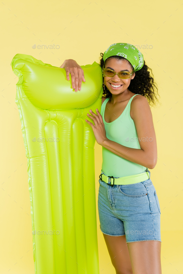 cheerful african american young woman standing with inflatable mattress  isolated on yellow Stock Photo by LightFieldStudios