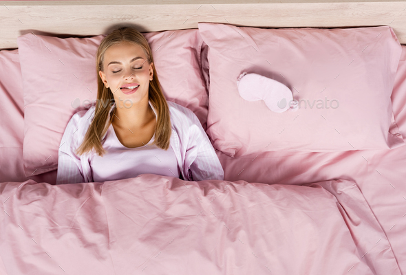 Top view of blonde woman sticking out tongue near sleep mask on bed