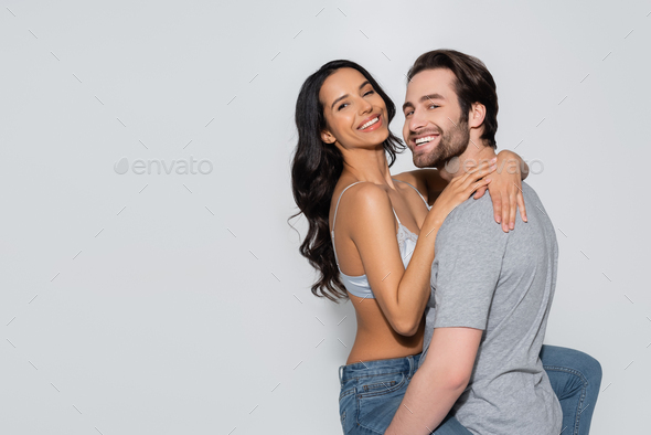 sexy girl in white bra looking at camera while embracing boyfriend sitting  on grey background Stock Photo by LightFieldStudios
