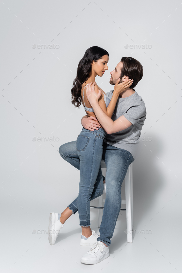 brunette woman in jeans and bra sitting on stool on grey Stock