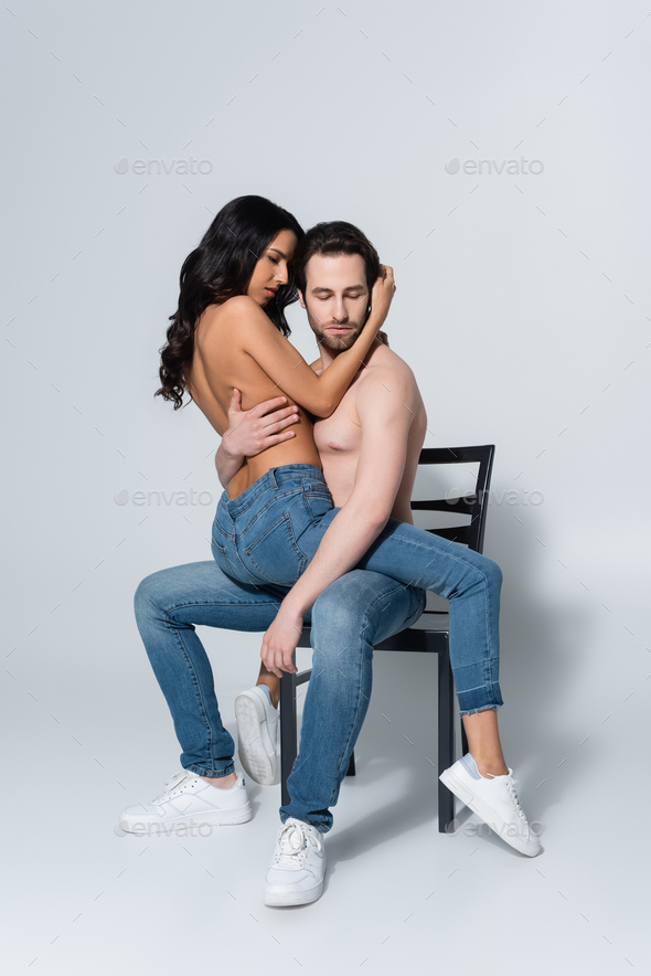 shirtless man in jeans sitting on chair with passionate girlfriend on grey  Stock Photo by LightFieldStudios