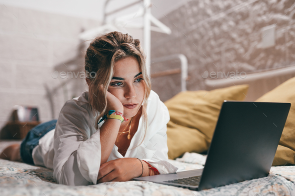 Close up of one young bored woman using laptop indoor at home lying on the bed