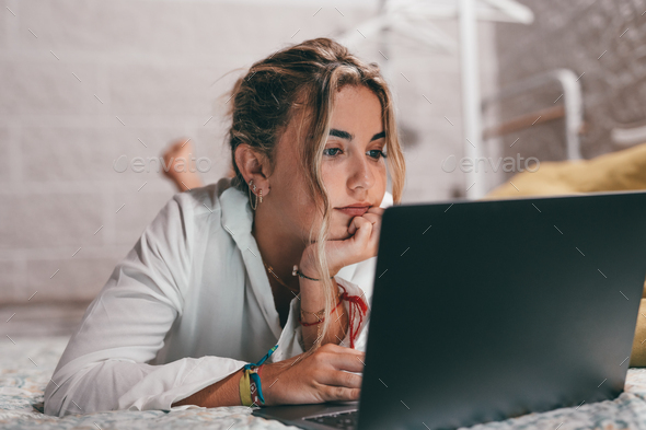 Close up of one young pretty woman using laptop indoor at home lying on the bed