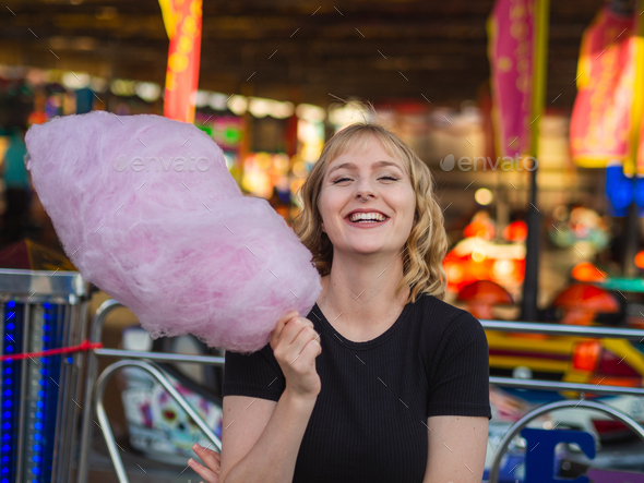 Young blonde female eating big cotton candy at an amusement park Stock  Photo by wirestock