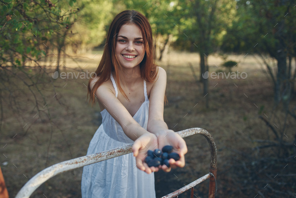 happy woman with a bunch of grapes leaned on an iron bed outdoors in the garden