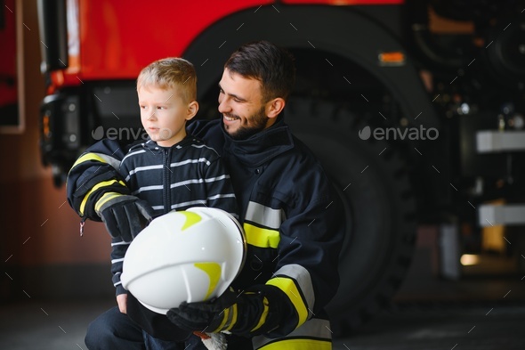 Dirty firefighter in uniform holding little saved boy standing on black  background.